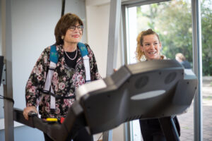 Senior woman using gait rehabilitation device with assistance from a physical therapist.